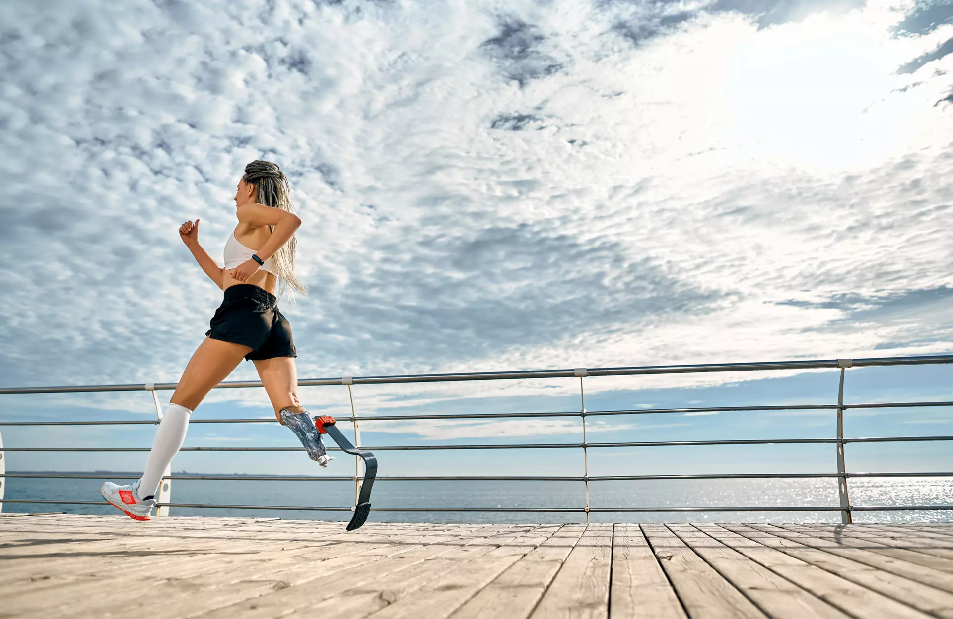 Sanitätskaufhaus Kellner - Relaunch 2025 - Stockmaterial - Orthopädie - Prothetik - junge Dame läuft mit sportlicher Beinprothese am Wasser entlang